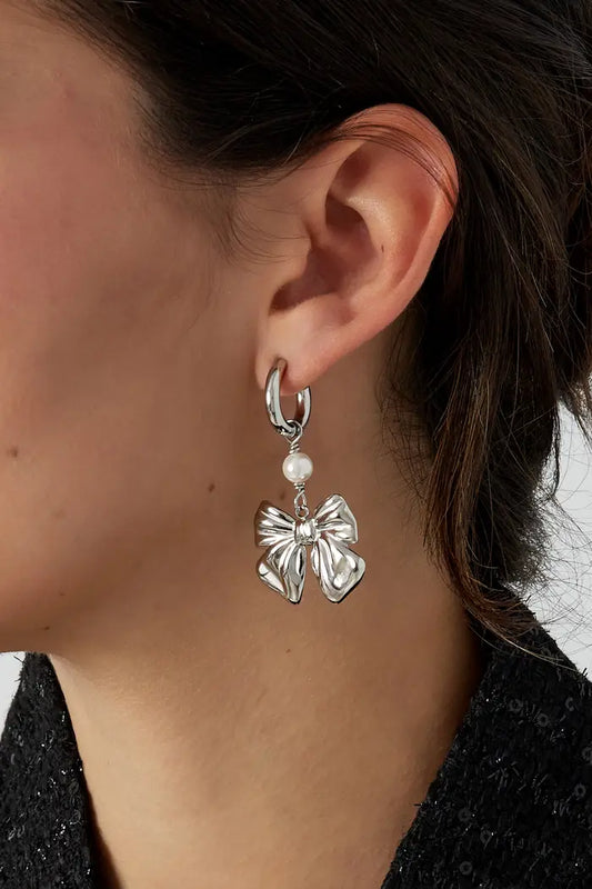 Oorbellen 'Baby Bow' in goud en zilver, met een verfijnd strikontwerp dat elegantie en speelsheid combineert, gepresenteerd op een neutrale achtergrond.